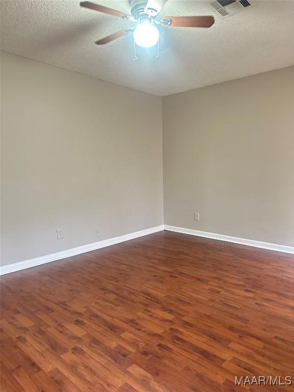 empty room with ceiling fan, dark wood-type flooring, and a textured ceiling