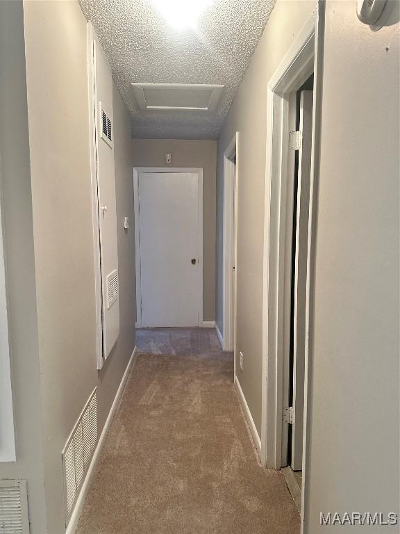 hall with light carpet and a textured ceiling