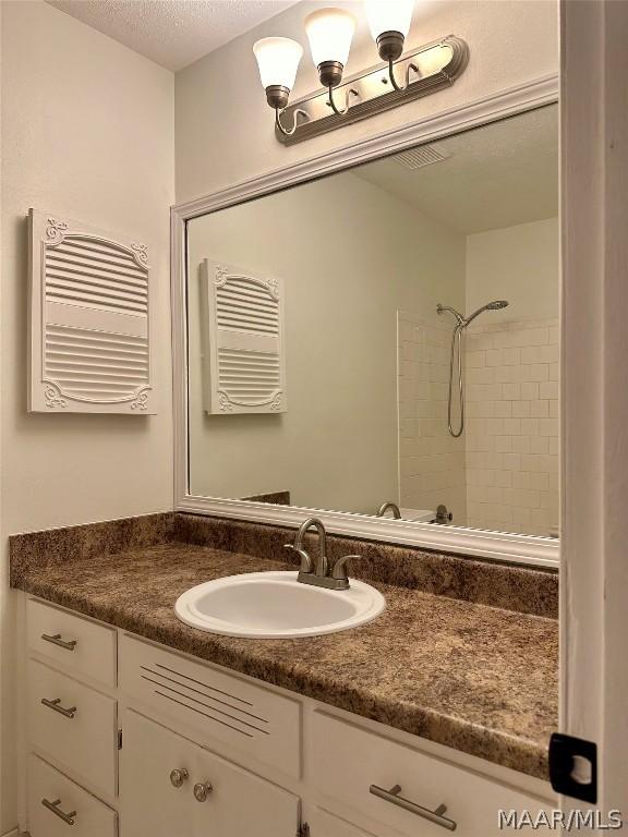 bathroom with a tile shower, vanity, and a textured ceiling