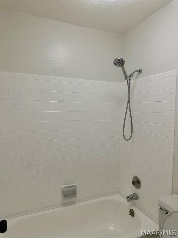 bathroom featuring tiled shower / bath combo and toilet