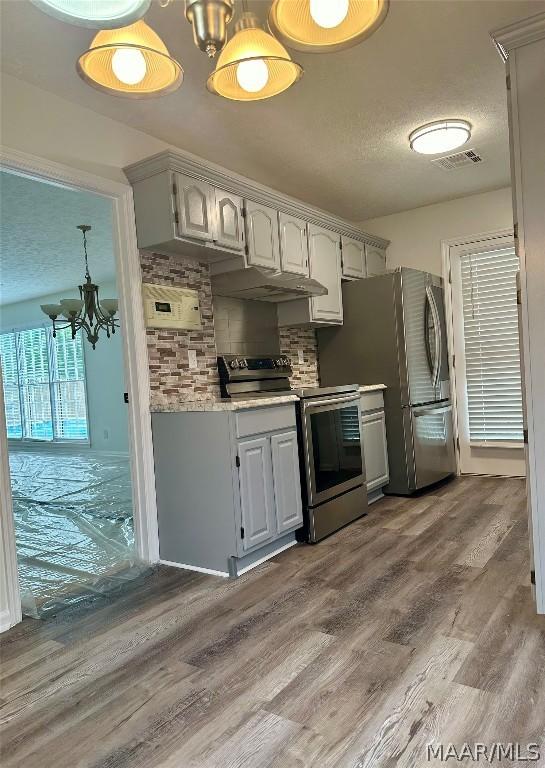 kitchen with decorative backsplash, a textured ceiling, stainless steel appliances, an inviting chandelier, and light hardwood / wood-style floors