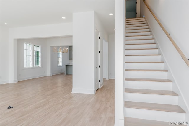 stairway with light hardwood / wood-style floors and a chandelier