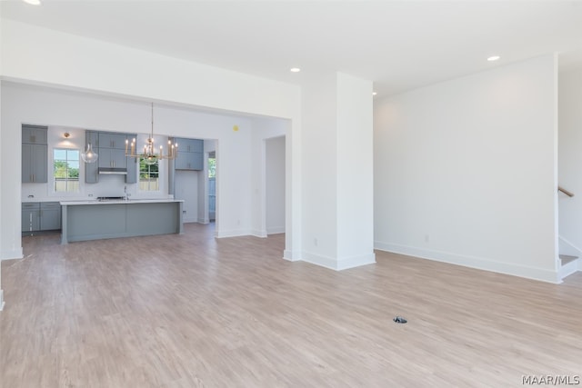 unfurnished living room featuring a notable chandelier and light wood-type flooring