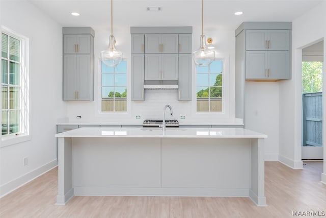 kitchen with hanging light fixtures, plenty of natural light, a center island with sink, and light hardwood / wood-style floors