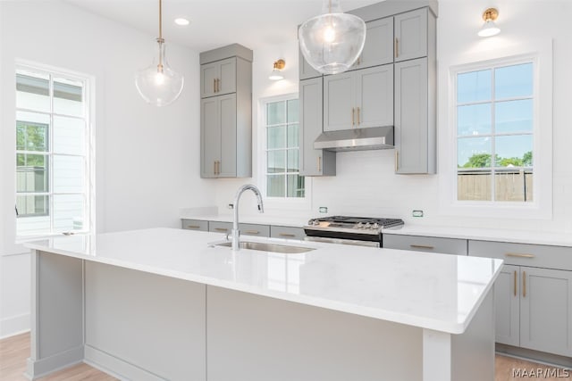 kitchen with gas range, a center island with sink, backsplash, and light wood-type flooring