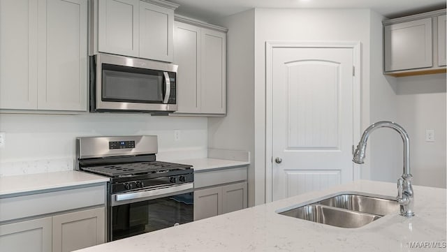 kitchen with stainless steel appliances, light stone countertops, sink, and gray cabinetry