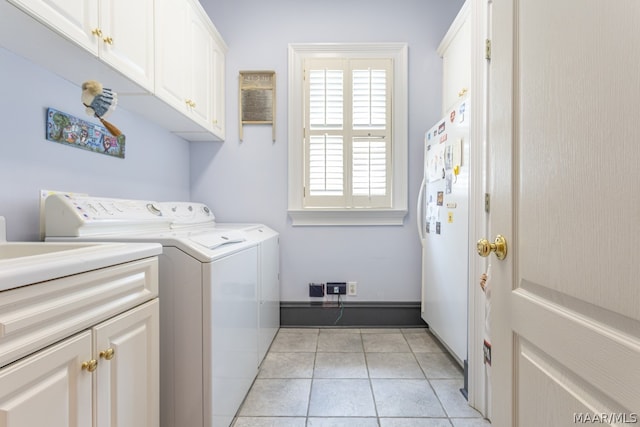 clothes washing area featuring cabinets, light tile floors, and washer and clothes dryer