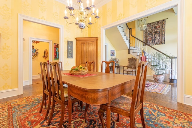 dining area with ornamental molding, wood-type flooring, a towering ceiling, and a notable chandelier