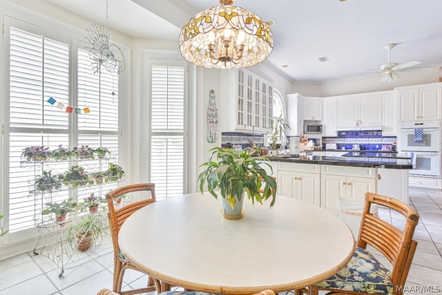 tiled dining room with ceiling fan with notable chandelier and crown molding