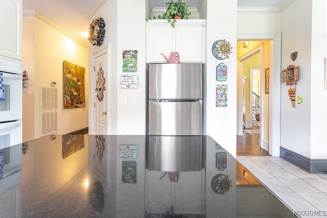 kitchen with crown molding, white cabinets, stainless steel fridge, and light tile flooring