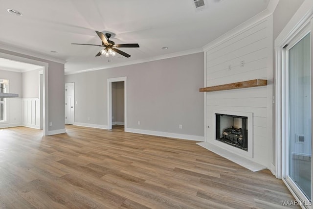 unfurnished living room featuring crown molding, a large fireplace, ceiling fan, and light hardwood / wood-style floors