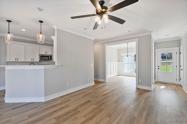 unfurnished living room featuring ceiling fan with notable chandelier, ornamental molding, and light wood-type flooring