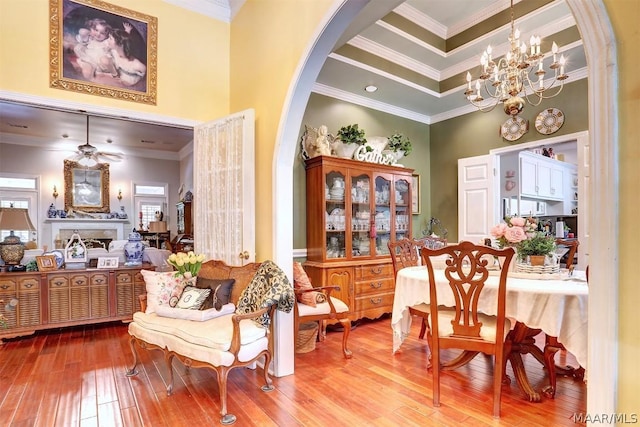 living area with ceiling fan with notable chandelier, light hardwood / wood-style floors, crown molding, and a high ceiling