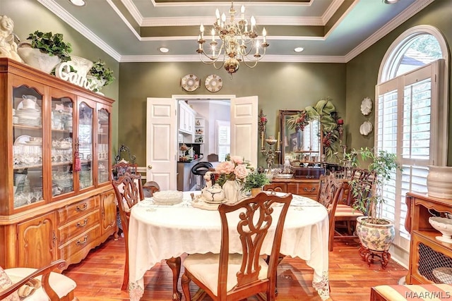 dining space featuring light wood-type flooring, a raised ceiling, and crown molding