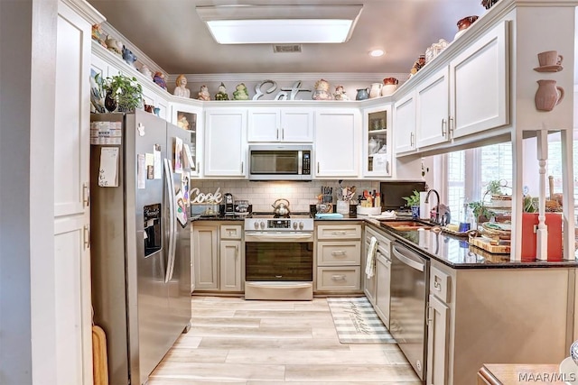 kitchen featuring stainless steel appliances, backsplash, dark stone countertops, crown molding, and light hardwood / wood-style floors