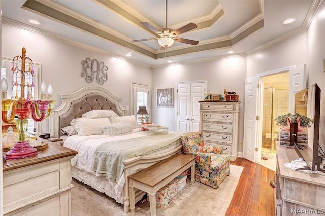 bedroom with ensuite bath, ceiling fan, light hardwood / wood-style floors, a tray ceiling, and ornamental molding