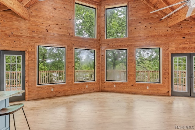 unfurnished living room featuring a towering ceiling, beamed ceiling, a healthy amount of sunlight, and light hardwood / wood-style floors