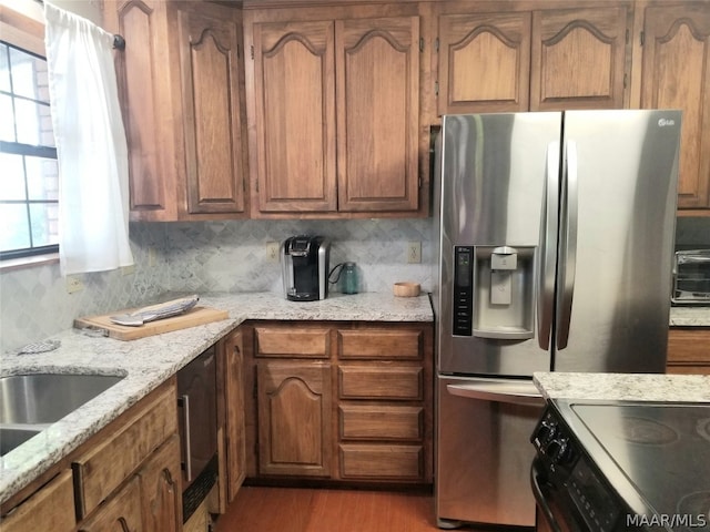 kitchen with electric range, light hardwood / wood-style floors, light stone counters, stainless steel refrigerator with ice dispenser, and tasteful backsplash