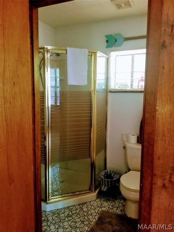 bathroom featuring a shower with door and toilet