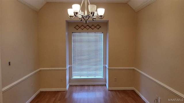 spare room featuring hardwood / wood-style floors, ornamental molding, an inviting chandelier, and vaulted ceiling