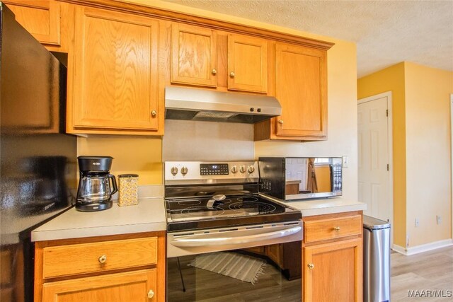 kitchen with stainless steel range with electric cooktop, black refrigerator, light hardwood / wood-style flooring, and a textured ceiling