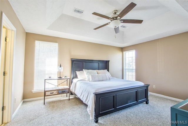 carpeted bedroom featuring a tray ceiling, baseboards, a ceiling fan, and visible vents