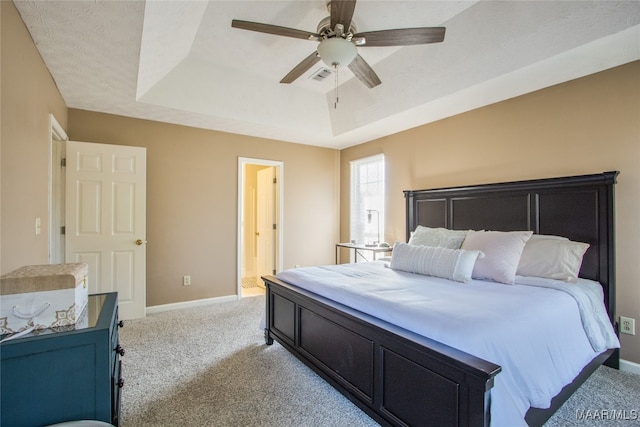 carpeted bedroom featuring a tray ceiling, ceiling fan, ensuite bathroom, and a textured ceiling