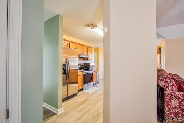 kitchen with stainless steel appliances, light hardwood / wood-style floors, light brown cabinetry, and a textured ceiling