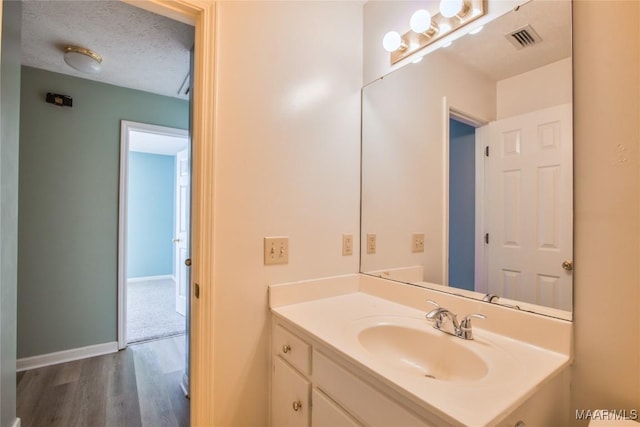 bathroom with visible vents, baseboards, a textured ceiling, vanity, and wood finished floors