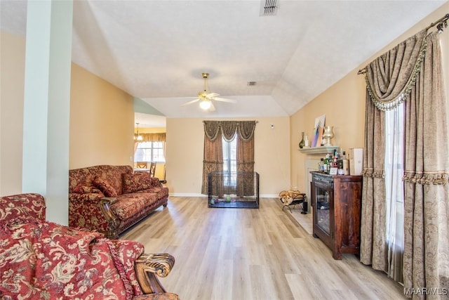 living area with a glass covered fireplace, light wood-type flooring, baseboards, visible vents, and ceiling fan