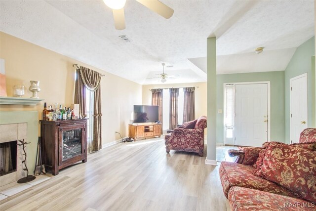 living room featuring a textured ceiling, a tile fireplace, lofted ceiling, light hardwood / wood-style flooring, and ceiling fan