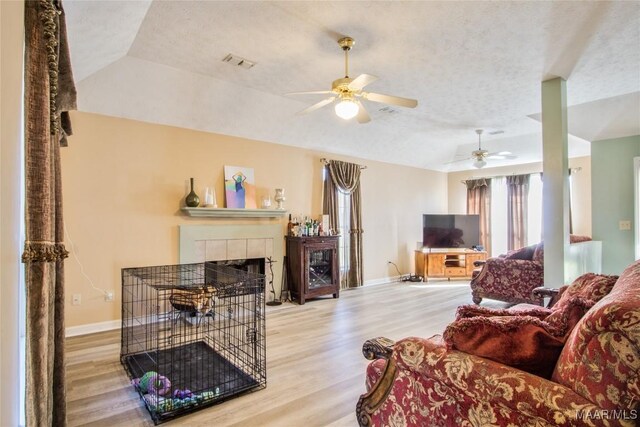 living room with a textured ceiling, a tiled fireplace, light hardwood / wood-style flooring, and ceiling fan