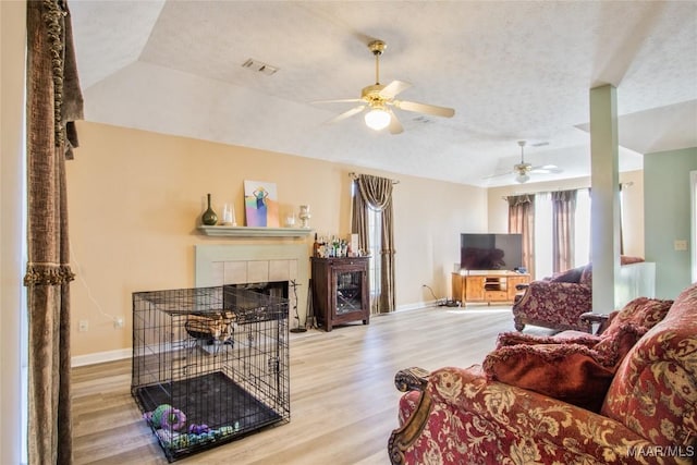living area with vaulted ceiling, a fireplace, visible vents, ceiling fan, and wood finished floors