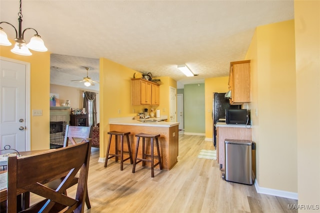 kitchen featuring light wood-type flooring, a tile fireplace, kitchen peninsula, and ceiling fan with notable chandelier