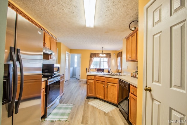 kitchen featuring light hardwood / wood-style floors, a textured ceiling, kitchen peninsula, black appliances, and decorative light fixtures