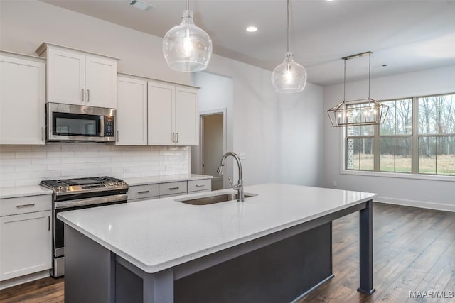 kitchen featuring appliances with stainless steel finishes, decorative light fixtures, white cabinetry, sink, and a center island with sink