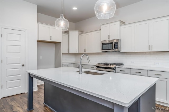 kitchen featuring pendant lighting, appliances with stainless steel finishes, sink, and a kitchen island with sink