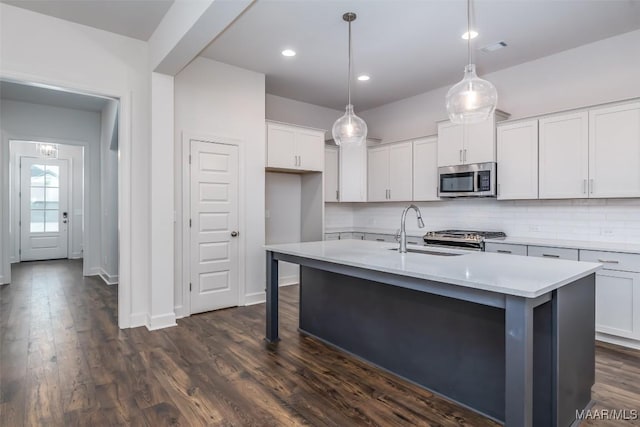 kitchen with appliances with stainless steel finishes, decorative light fixtures, sink, white cabinets, and a kitchen island with sink