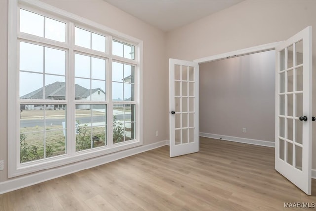 empty room with french doors, baseboards, and light wood finished floors