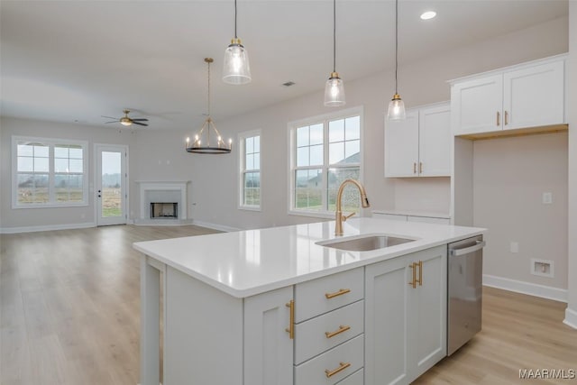 kitchen with a kitchen island with sink, a fireplace with raised hearth, a sink, light countertops, and dishwasher