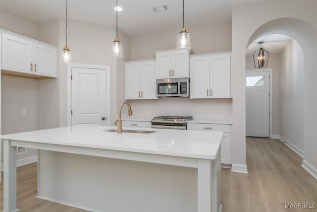 kitchen featuring light wood finished floors, visible vents, arched walkways, stainless steel appliances, and a sink