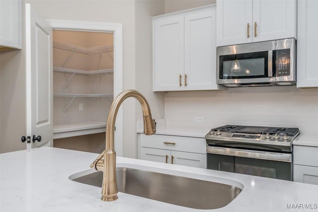 kitchen featuring white cabinets, backsplash, appliances with stainless steel finishes, and a sink