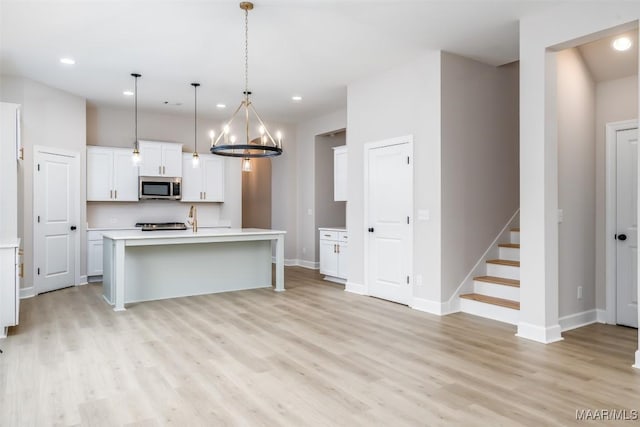 kitchen with stainless steel microwave, white cabinetry, light countertops, and light wood-style floors