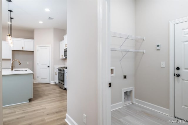 washroom with visible vents, hookup for an electric dryer, laundry area, light wood-style flooring, and a sink