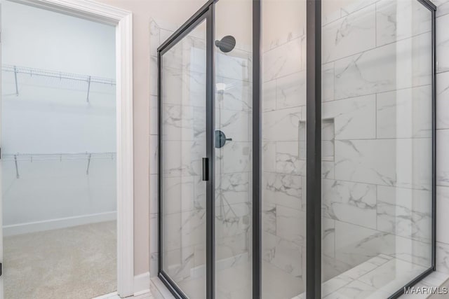 bathroom featuring a marble finish shower, a spacious closet, and baseboards