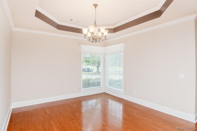 empty room with wood-type flooring, ornamental molding, a tray ceiling, and an inviting chandelier