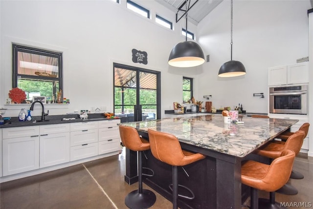 kitchen with stainless steel oven, dark stone countertops, a towering ceiling, decorative light fixtures, and white cabinets