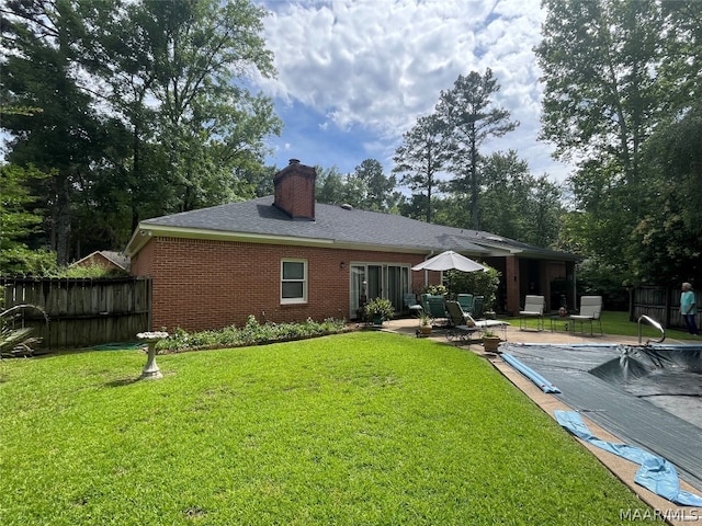 rear view of property featuring a patio, brick siding, a lawn, and fence