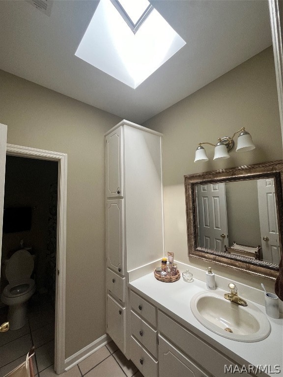 bathroom with a skylight, baseboards, toilet, tile patterned floors, and vanity