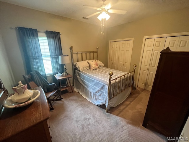 carpeted bedroom featuring a ceiling fan, visible vents, and multiple closets